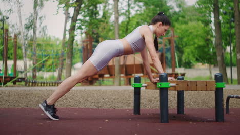 Female-athlete-doing-bench-push-ups-for-strength-workout-at-city-park-in-summer.-Sporty-woman-training-outdoor